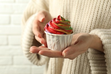 Photo of Woman holding delicious cupcake with colorful cream against white brick wall, closeup