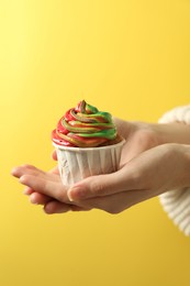 Photo of Woman holding delicious cupcake with colorful cream on yellow background, closeup