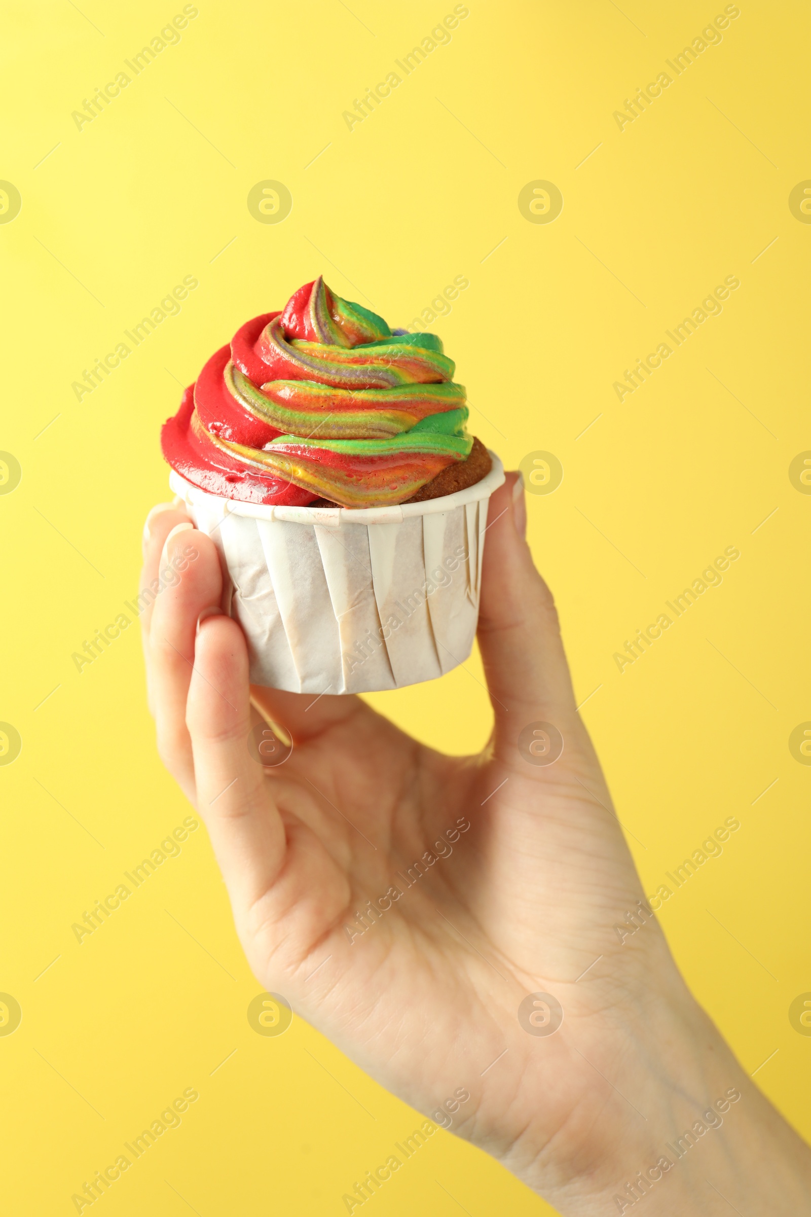 Photo of Woman holding delicious cupcake with colorful cream on yellow background, closeup