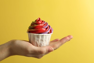 Photo of Woman holding delicious cupcake with colorful cream on yellow background, closeup