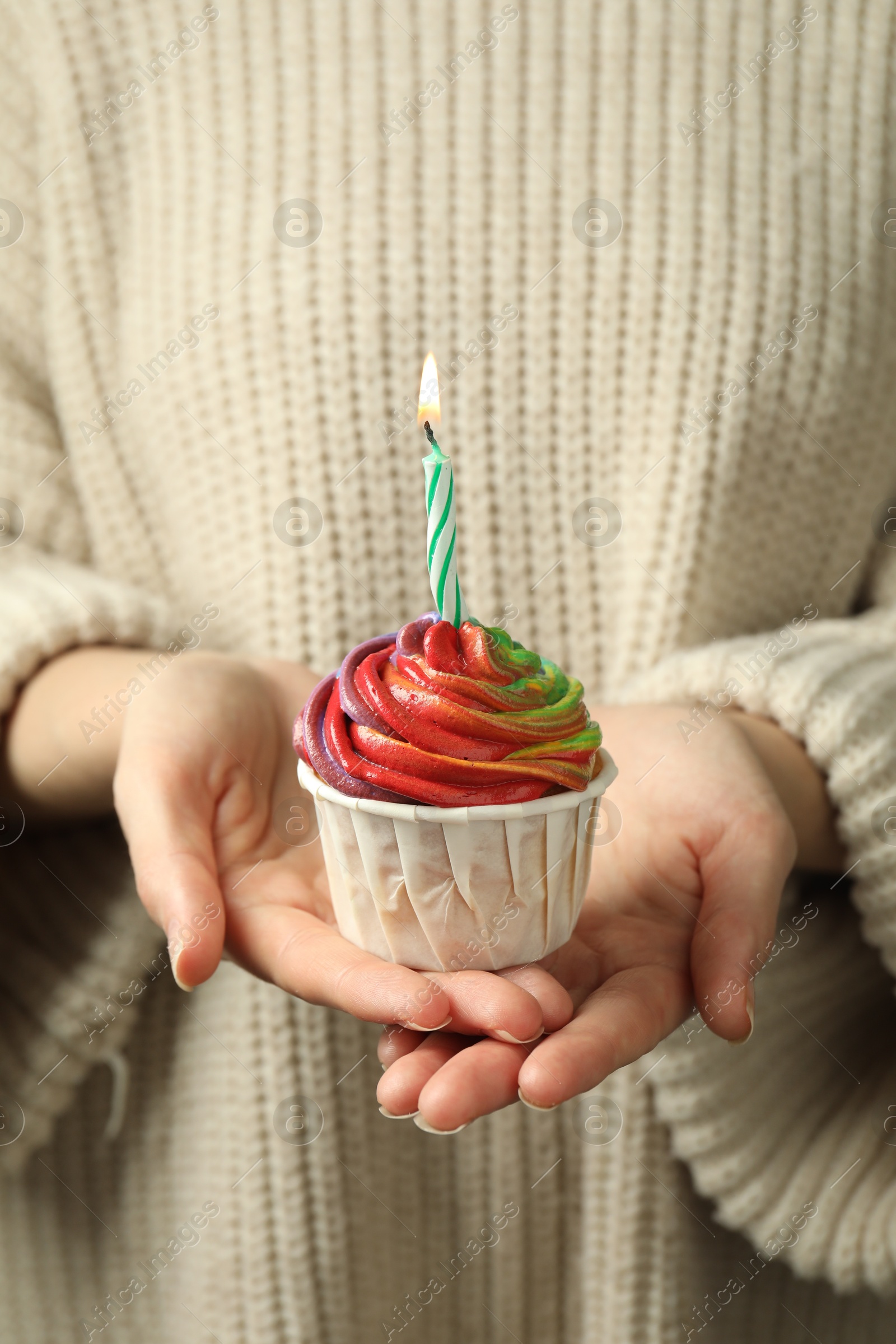 Photo of Woman holding delicious cupcake with colorful cream and burning candle, closeup