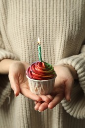 Photo of Woman holding delicious cupcake with colorful cream and burning candle, closeup