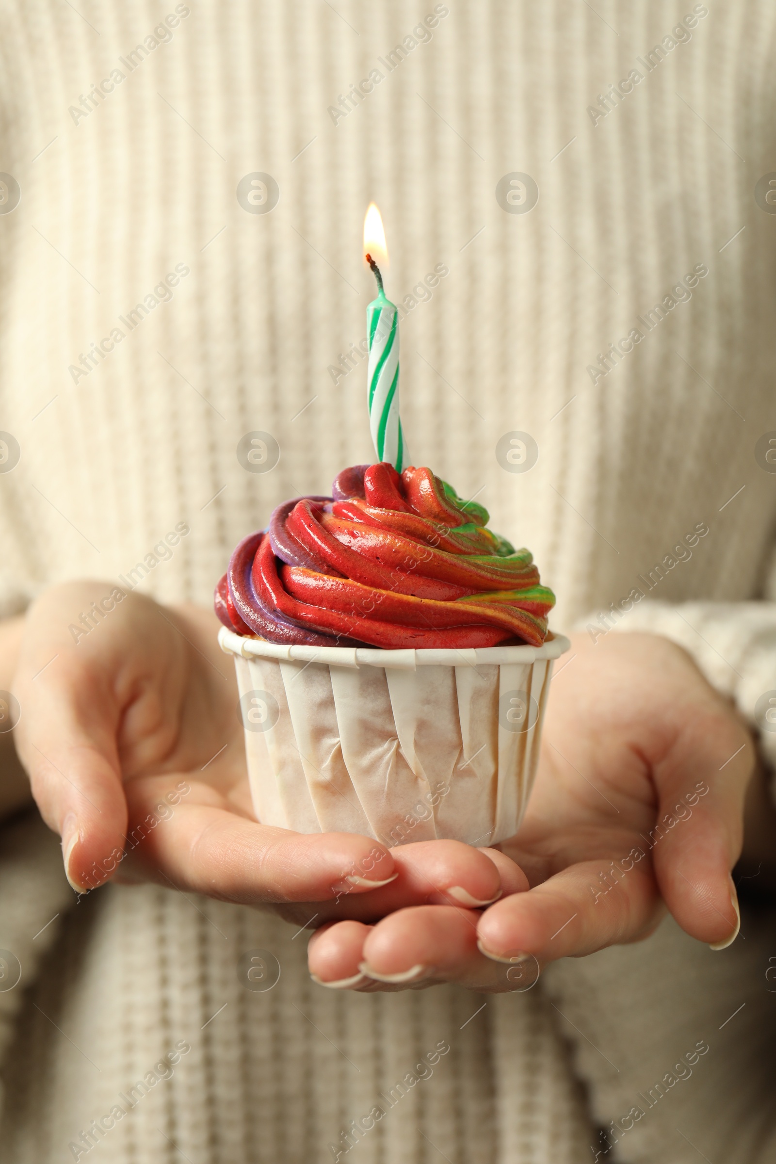 Photo of Woman holding delicious cupcake with colorful cream and burning candle, closeup