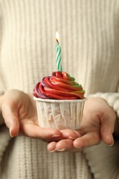 Photo of Woman holding delicious cupcake with colorful cream and burning candle, closeup