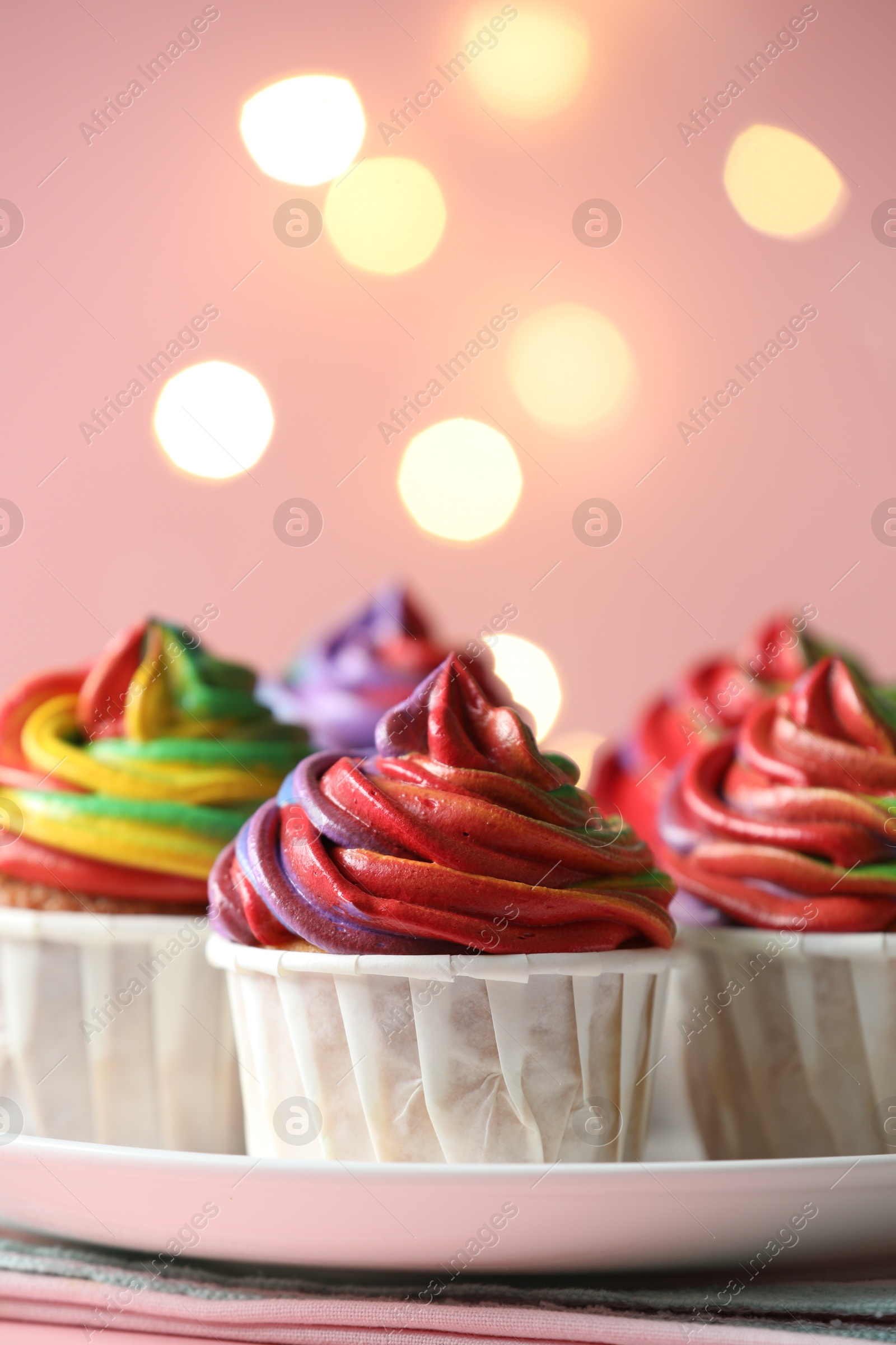 Photo of Delicious cupcakes with colorful cream on table against pink background, closeup. Bokeh effect