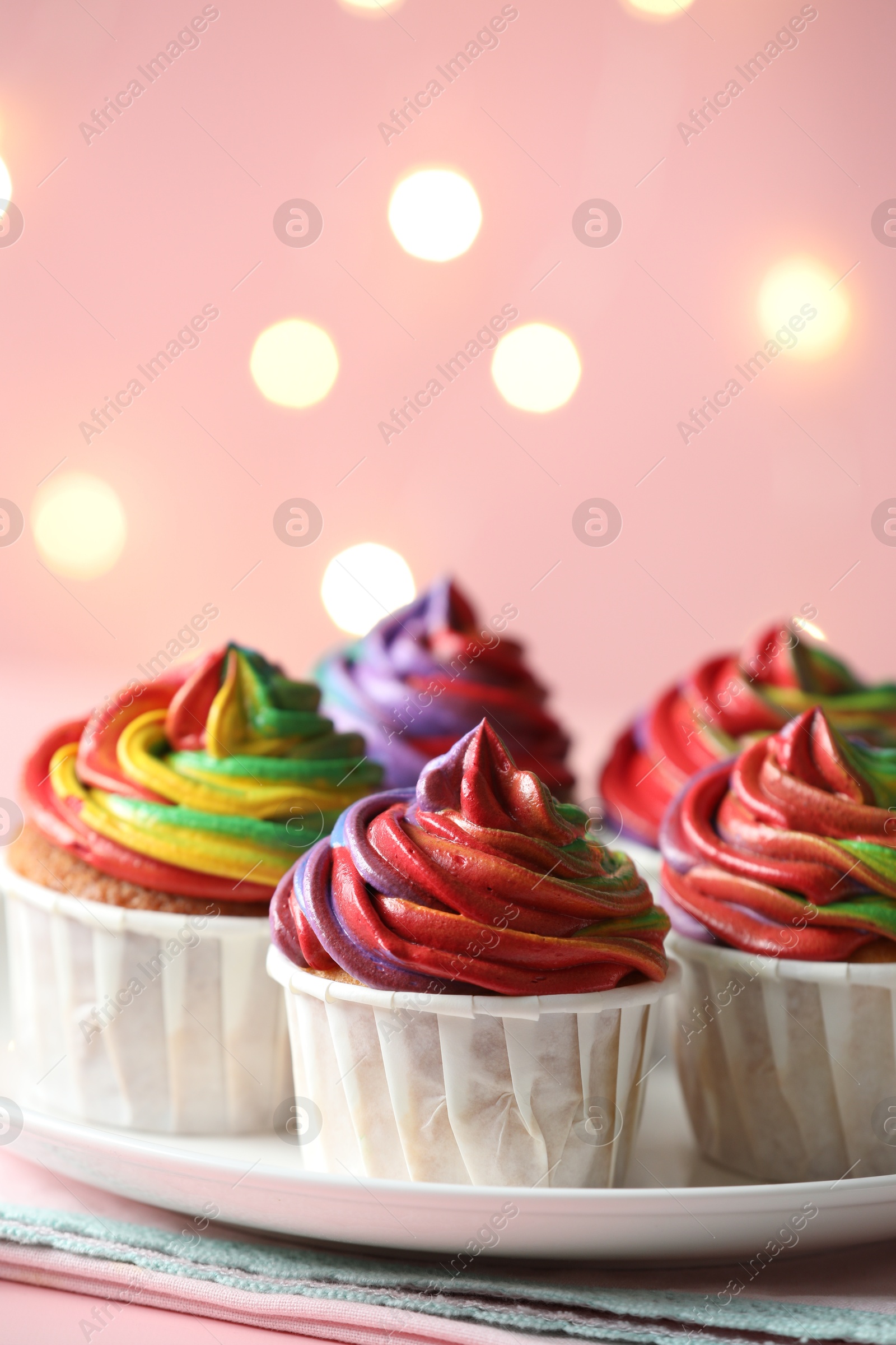 Photo of Delicious cupcakes with colorful cream on table against pink background, closeup and space for text. Bokeh effect