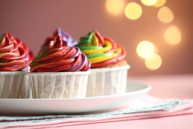 Photo of Delicious cupcakes with colorful cream on table against pink background, closeup. Bokeh effect