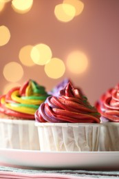 Photo of Delicious cupcakes with colorful cream on table against pink background, closeup and space for text. Bokeh effect