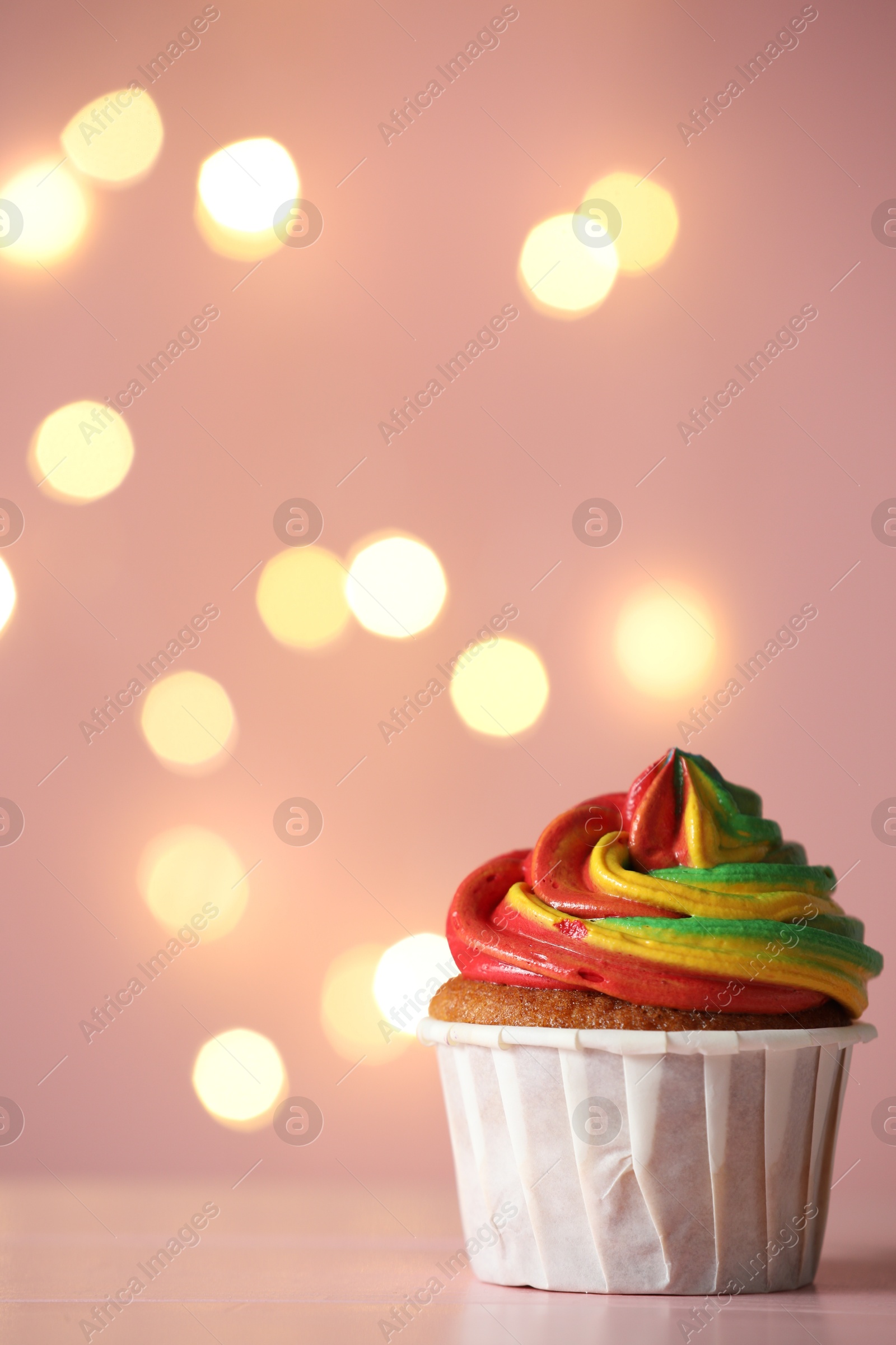 Photo of Delicious cupcake with colorful cream on table against pink background, closeup and space for text. Bokeh effect