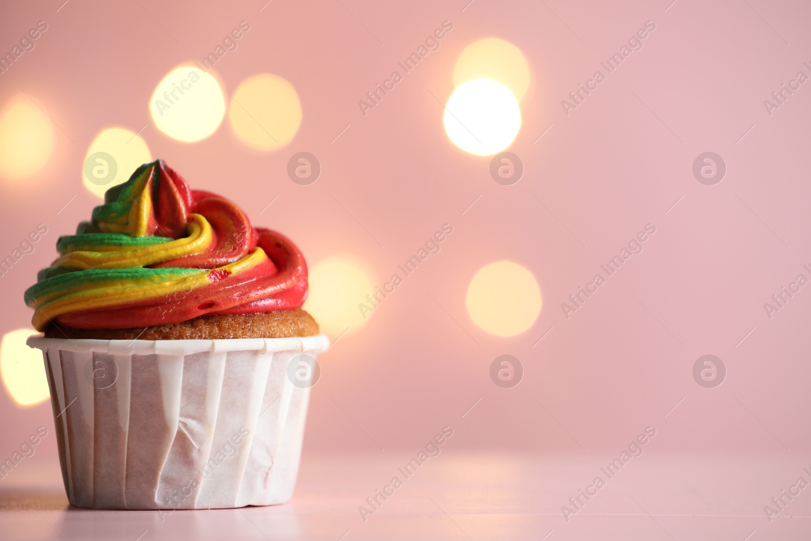 Photo of Delicious cupcake with colorful cream on table against pink background, closeup and space for text. Bokeh effect