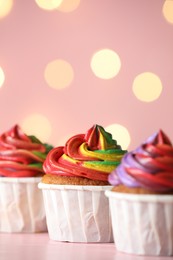 Photo of Delicious cupcakes with colorful cream on table against pink background, closeup. Bokeh effect