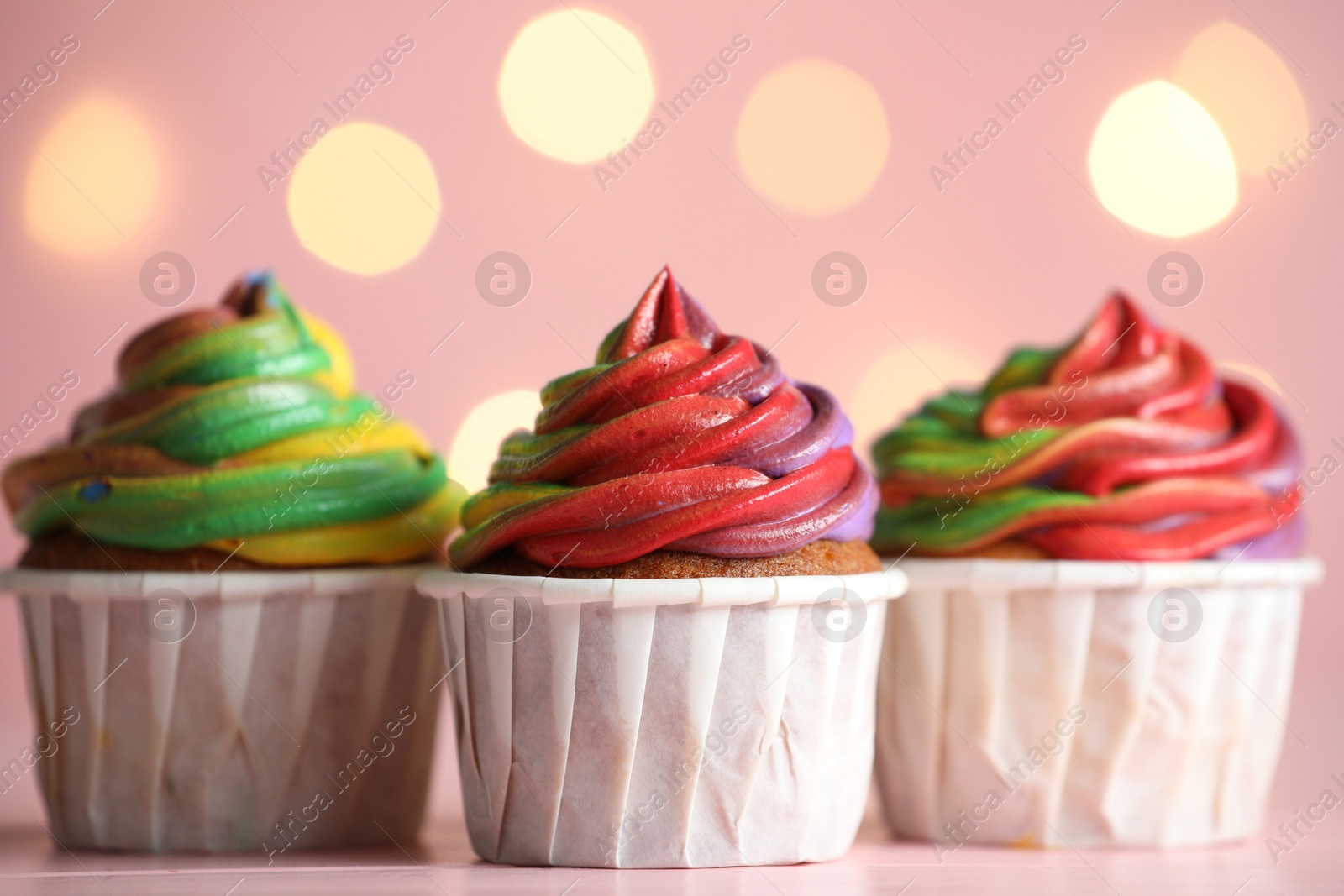 Photo of Delicious cupcakes with colorful cream on table against pink background, closeup. Bokeh effect