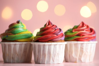 Photo of Delicious cupcakes with colorful cream on table against pink background, closeup. Bokeh effect