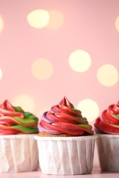 Photo of Delicious cupcakes with colorful cream on table against pink background, closeup and space for text. Bokeh effect