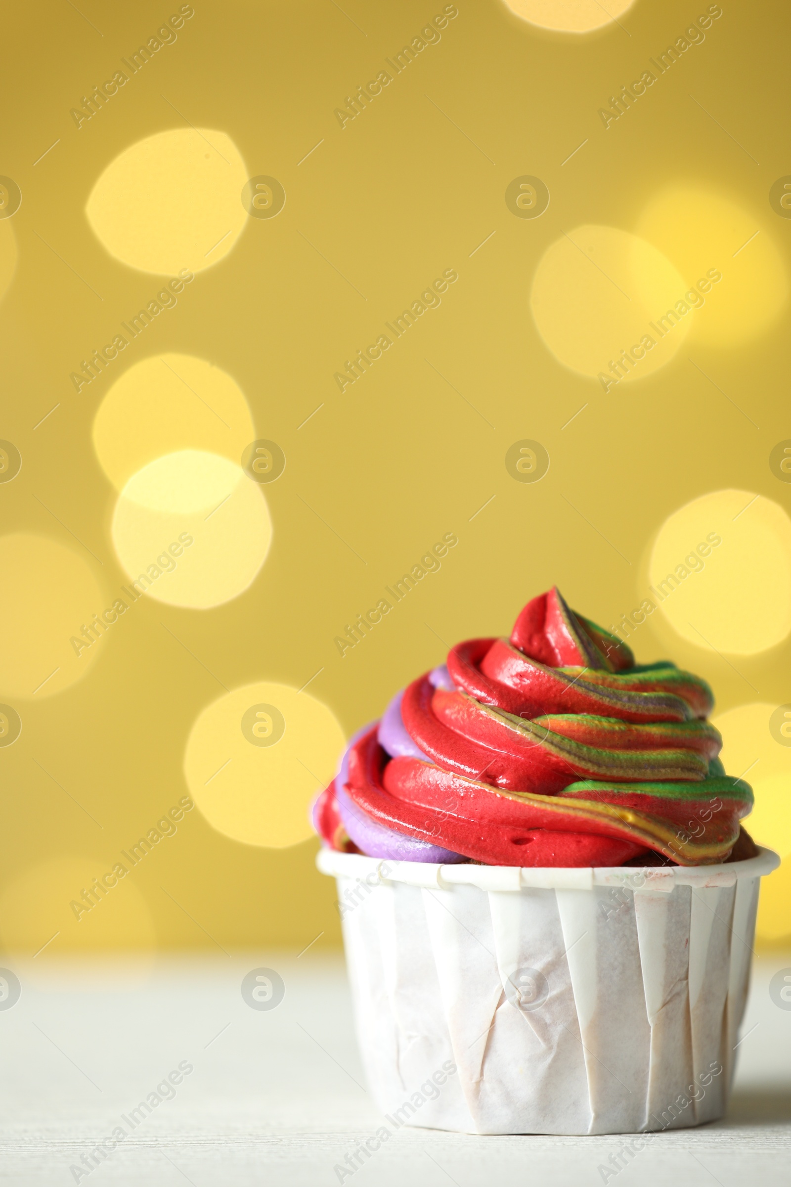 Photo of Delicious cupcake with colorful cream on white table against golden background, closeup and space for text. Bokeh effect