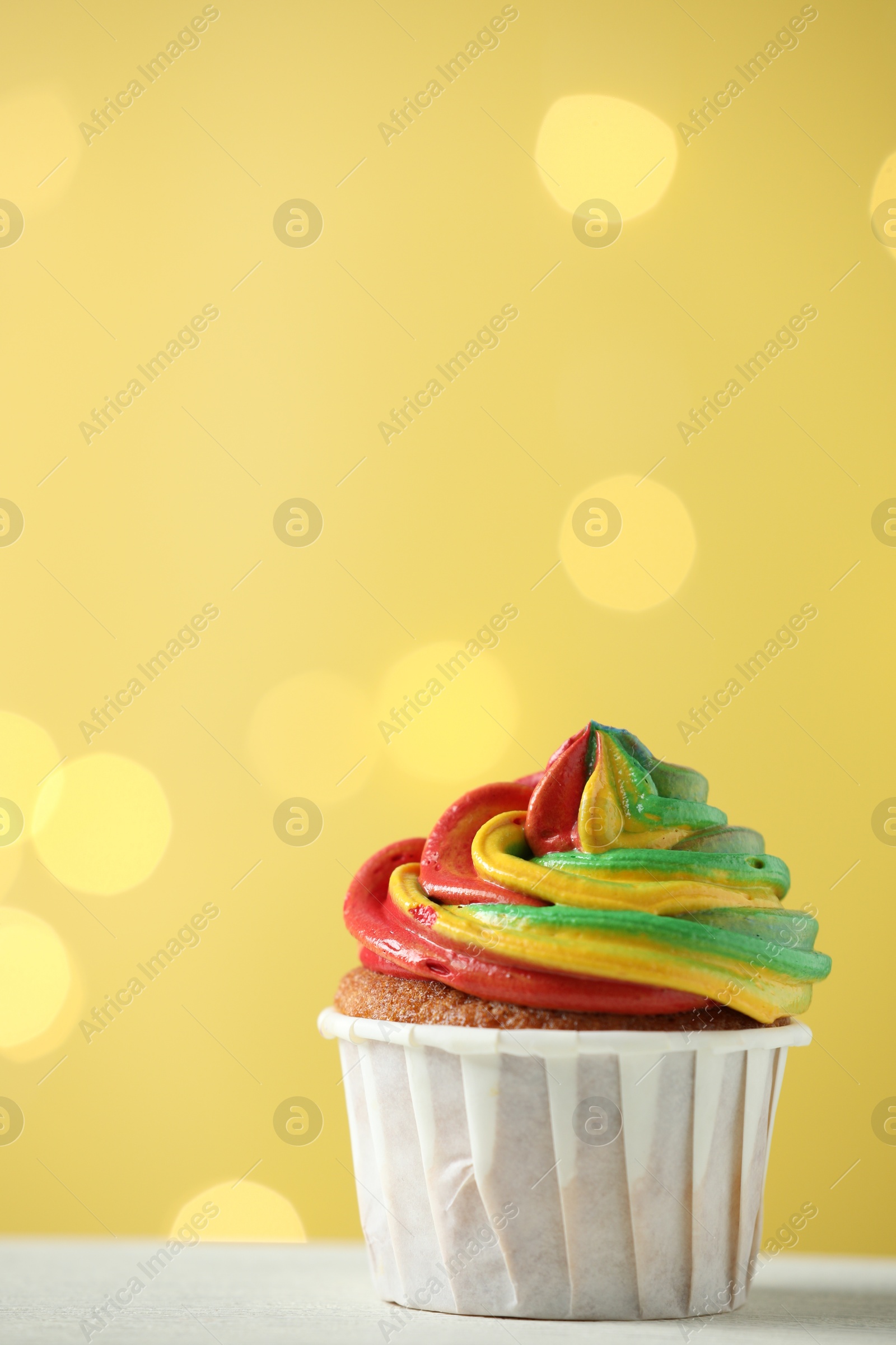 Photo of Delicious cupcake with colorful cream on white table against golden background, closeup and space for text. Bokeh effect