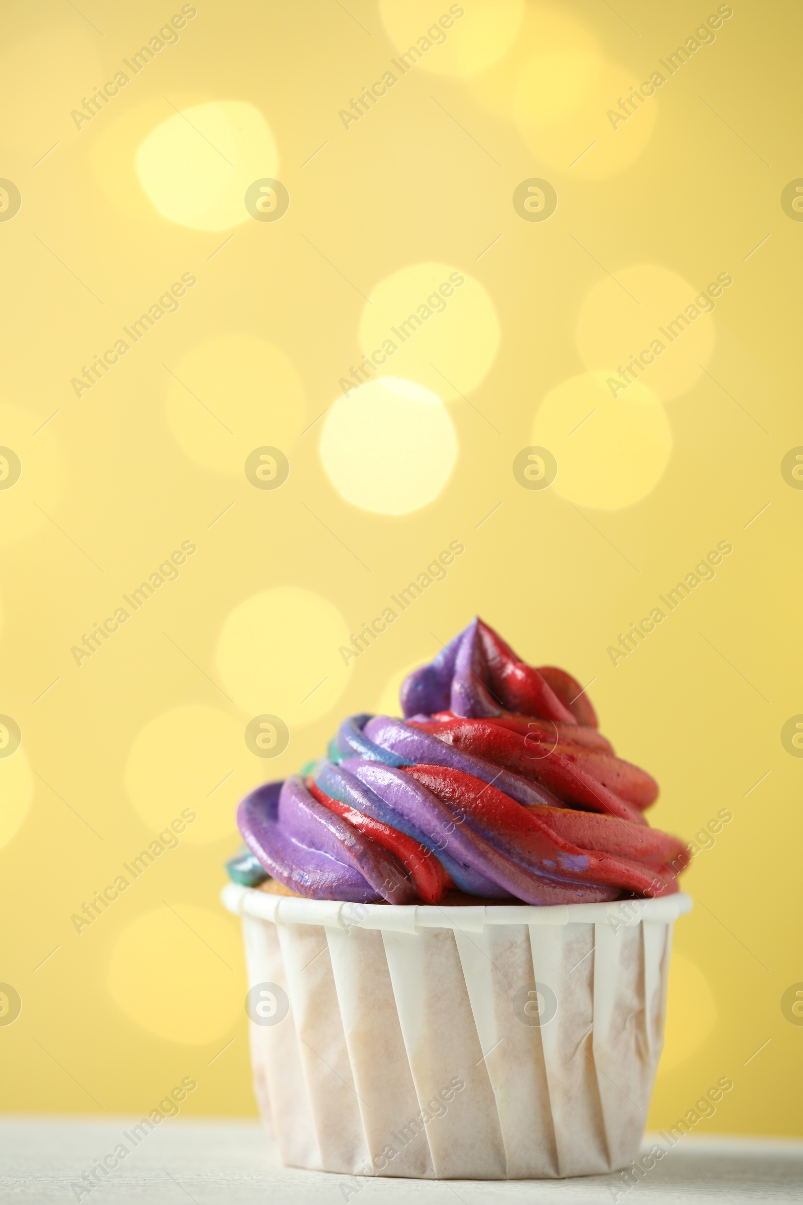 Photo of Delicious cupcake with colorful cream on white table against golden background, closeup and space for text. Bokeh effect