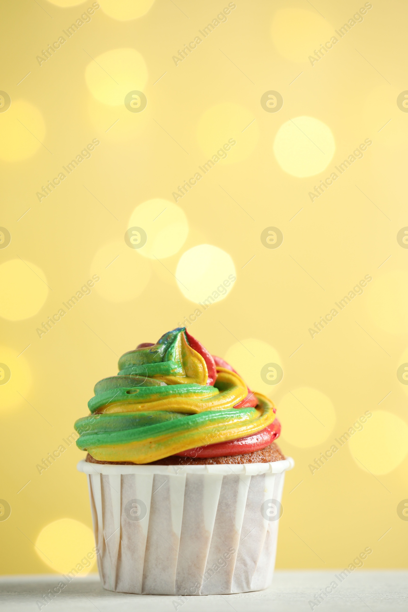 Photo of Delicious cupcake with colorful cream on white table against golden background, closeup and space for text. Bokeh effect