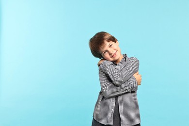 Cute little boy hugging himself on light blue background, space for text