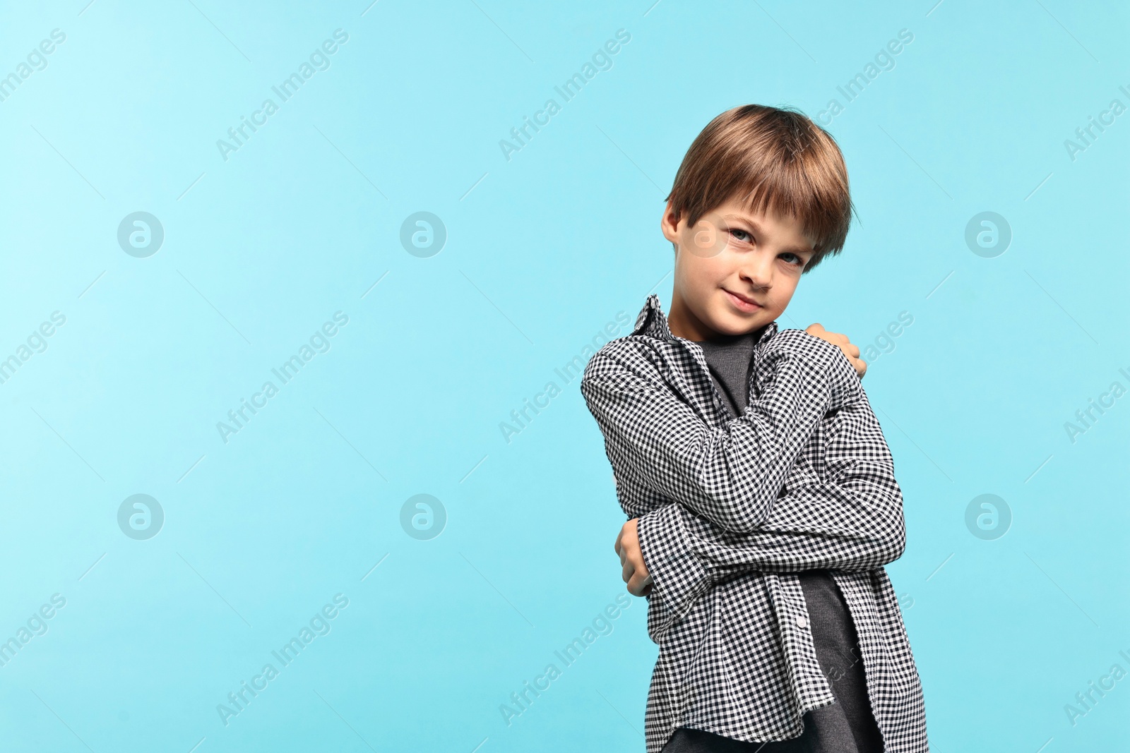 Photo of Cute little boy hugging himself on light blue background, space for text