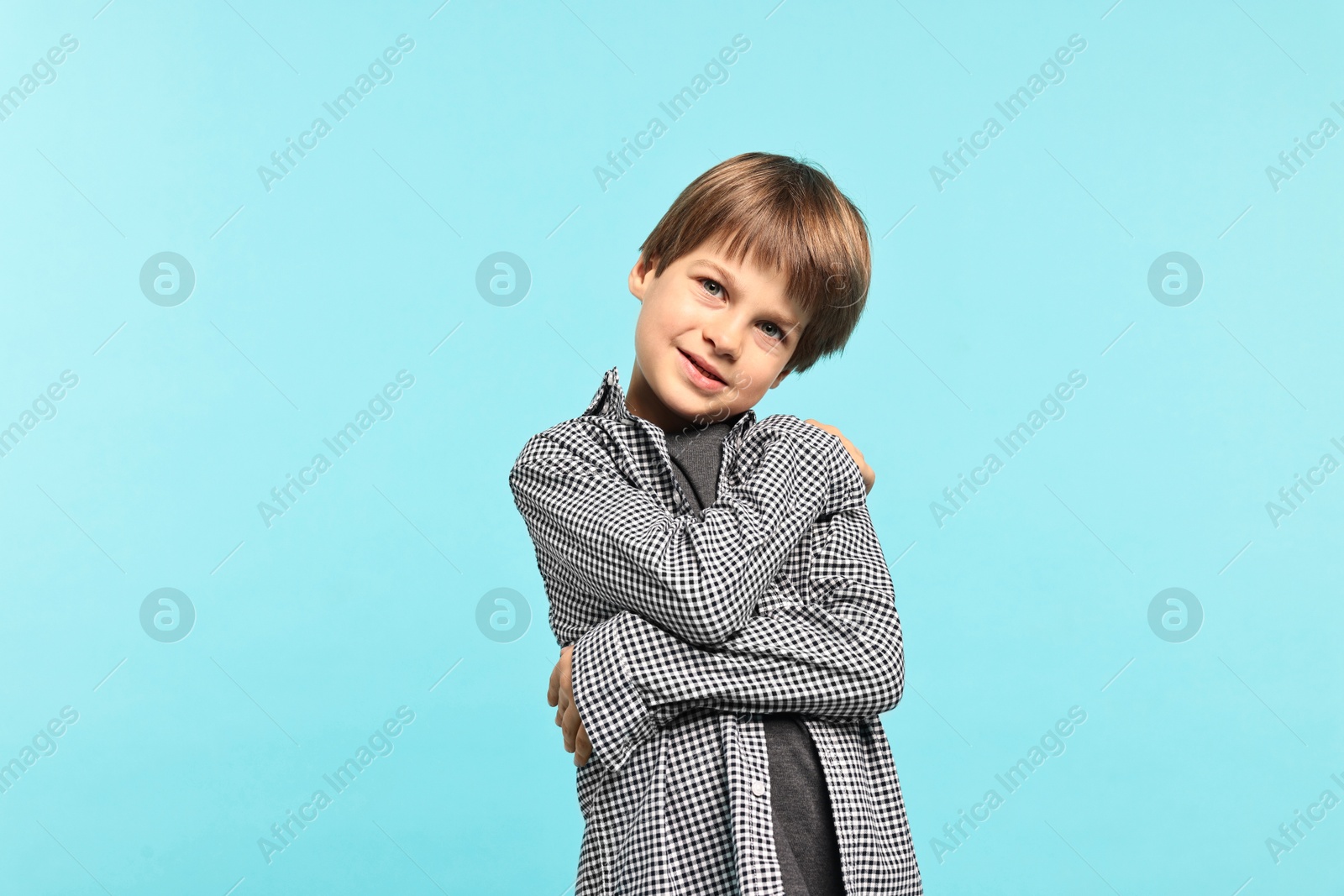 Photo of Cute little boy hugging himself on light blue background