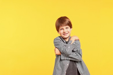 Photo of Cute little boy hugging himself on yellow background, space for text