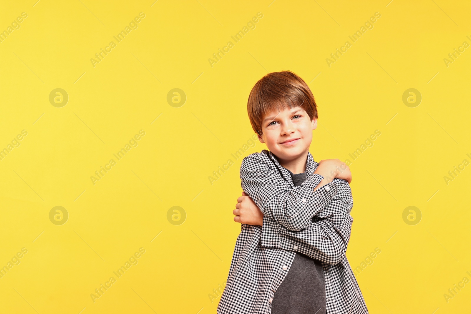 Photo of Cute little boy hugging himself on yellow background, space for text