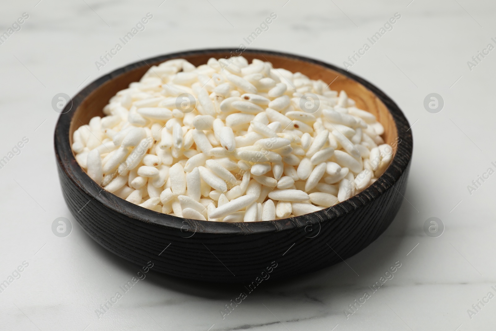 Photo of Puffed rice in bowl on white marble table, closeup