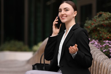 Photo of Woman in stylish formal suit talking on phone outdoors. Space for text