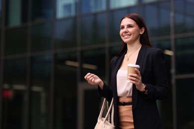 Woman in stylish formal suit with cup of coffee outdoors. Space for text