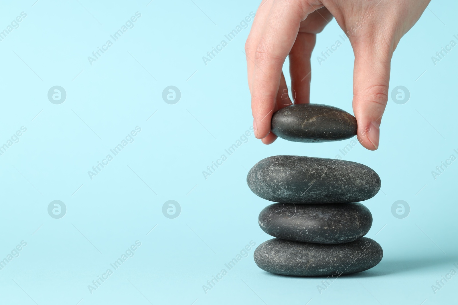 Photo of Harmony and life balance. Woman making stack of stones on light blue background, closeup. Space for text