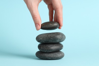 Photo of Woman making stack of stones on light blue background, closeup. Harmony and life balance