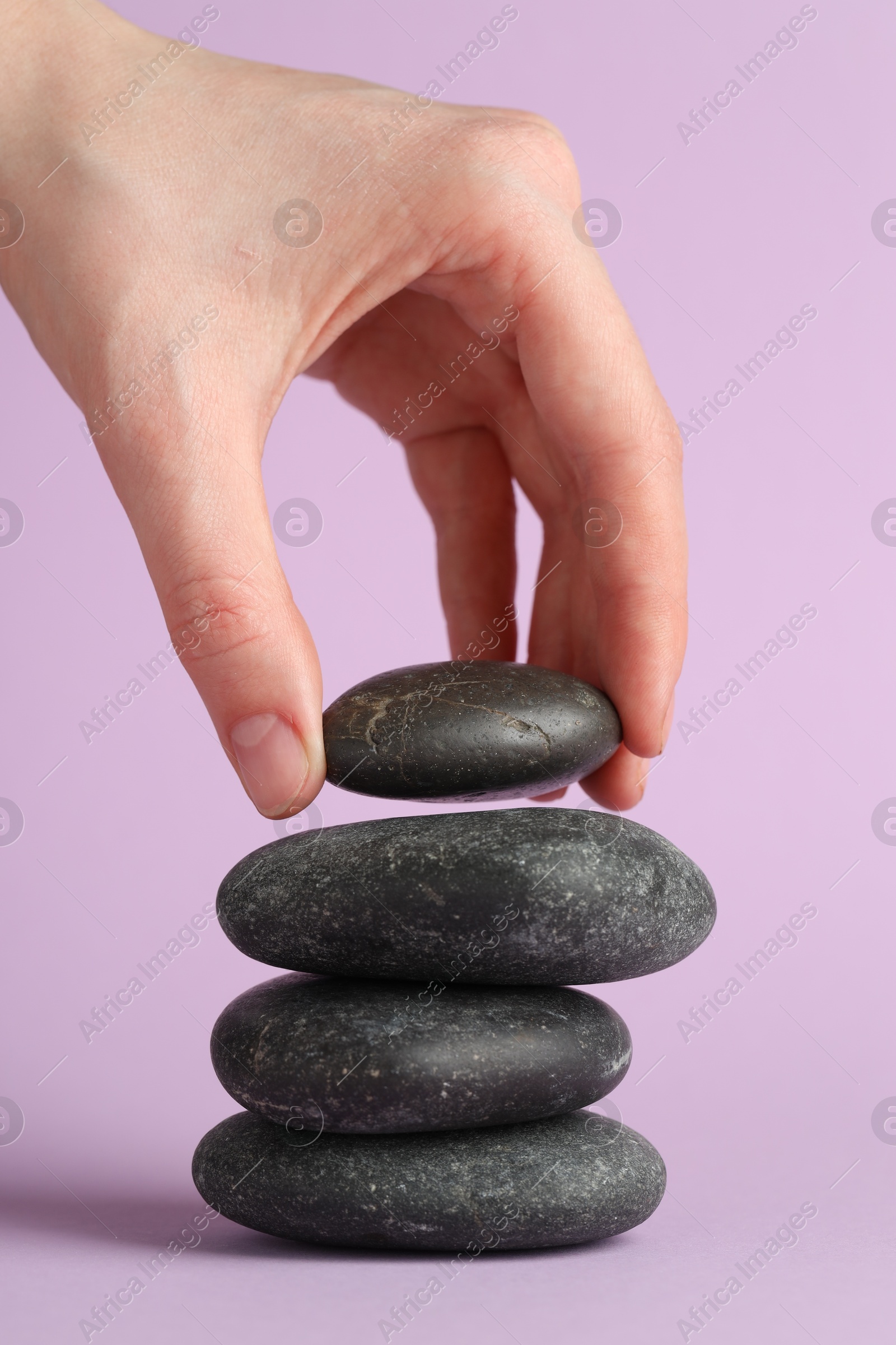 Photo of Woman making stack of stones on lilac background, closeup. Harmony and life balance