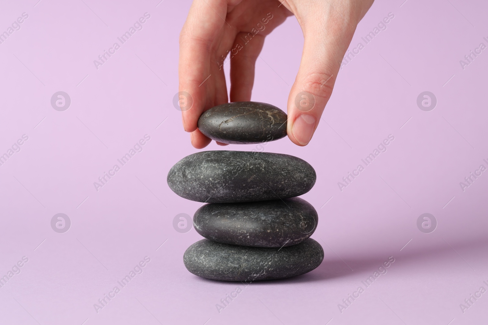 Photo of Woman making stack of stones on lilac background, closeup. Harmony and life balance