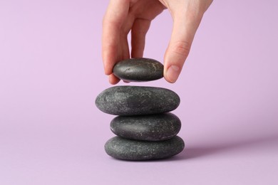 Photo of Woman making stack of stones on lilac background, closeup. Harmony and life balance