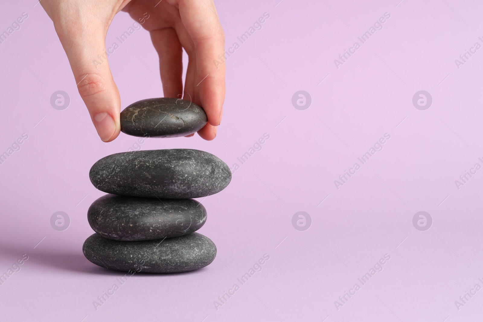 Photo of Harmony and life balance. Woman making stack of stones on lilac background, closeup. Space for text