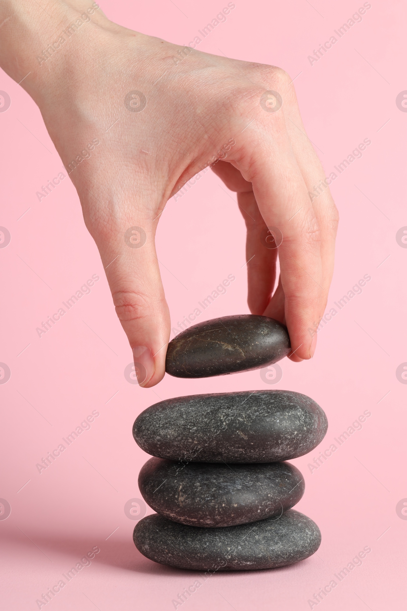 Photo of Woman making stack of stones on pink background, closeup. Harmony and life balance