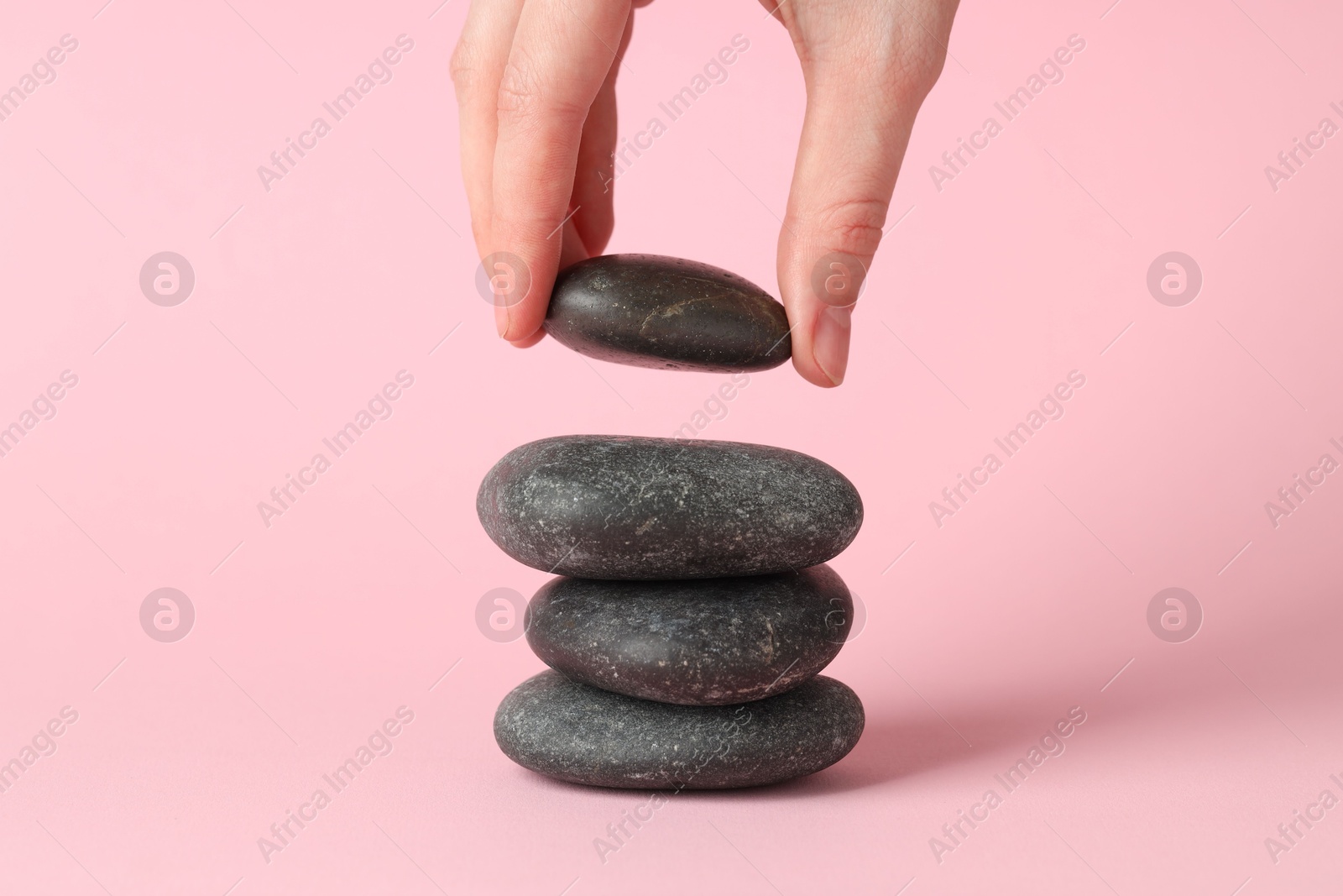 Photo of Woman making stack of stones on pink background, closeup. Harmony and life balance