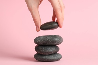 Photo of Woman making stack of stones on pink background, closeup. Harmony and life balance