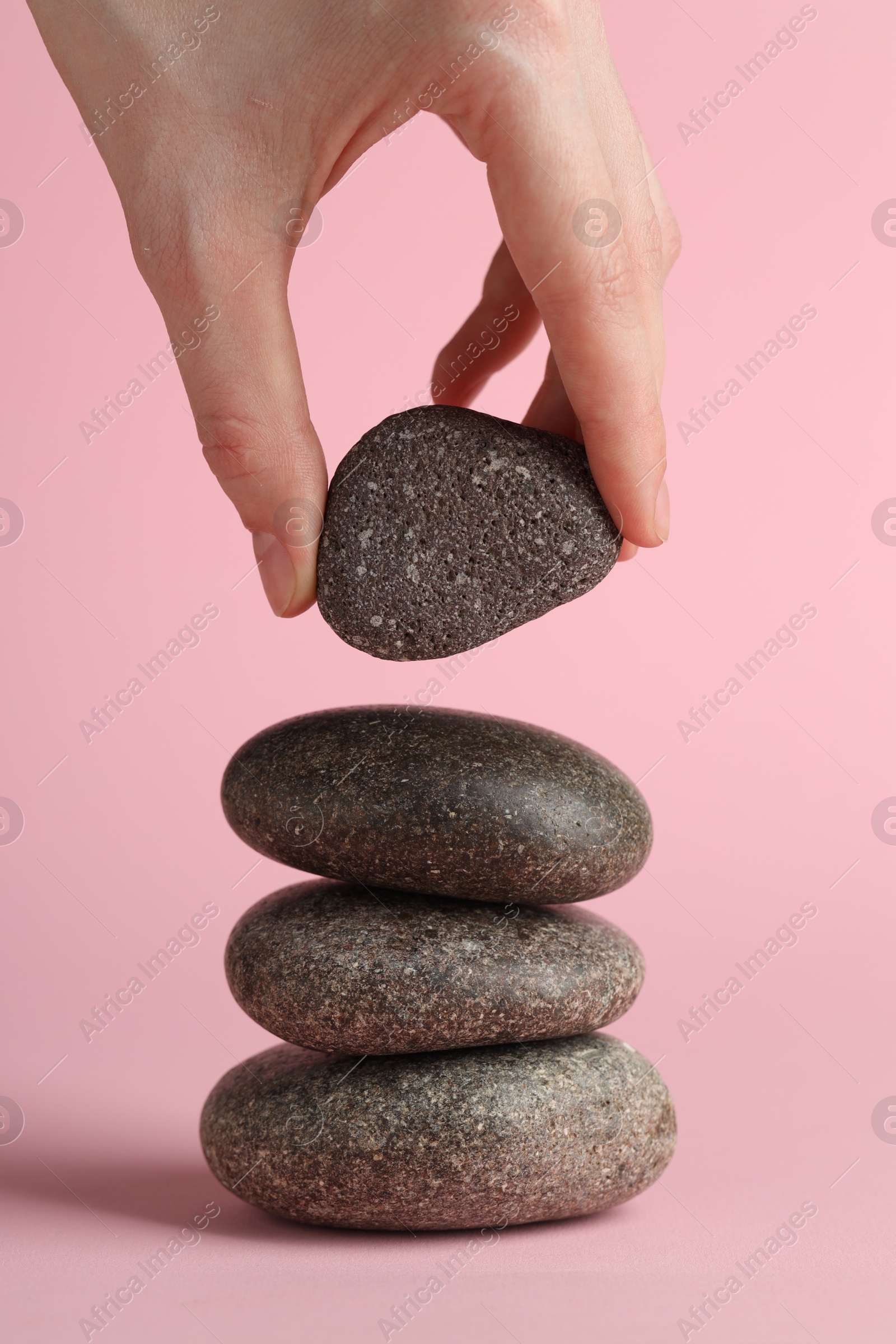 Photo of Woman making stack of stones on pink background, closeup. Harmony and life balance