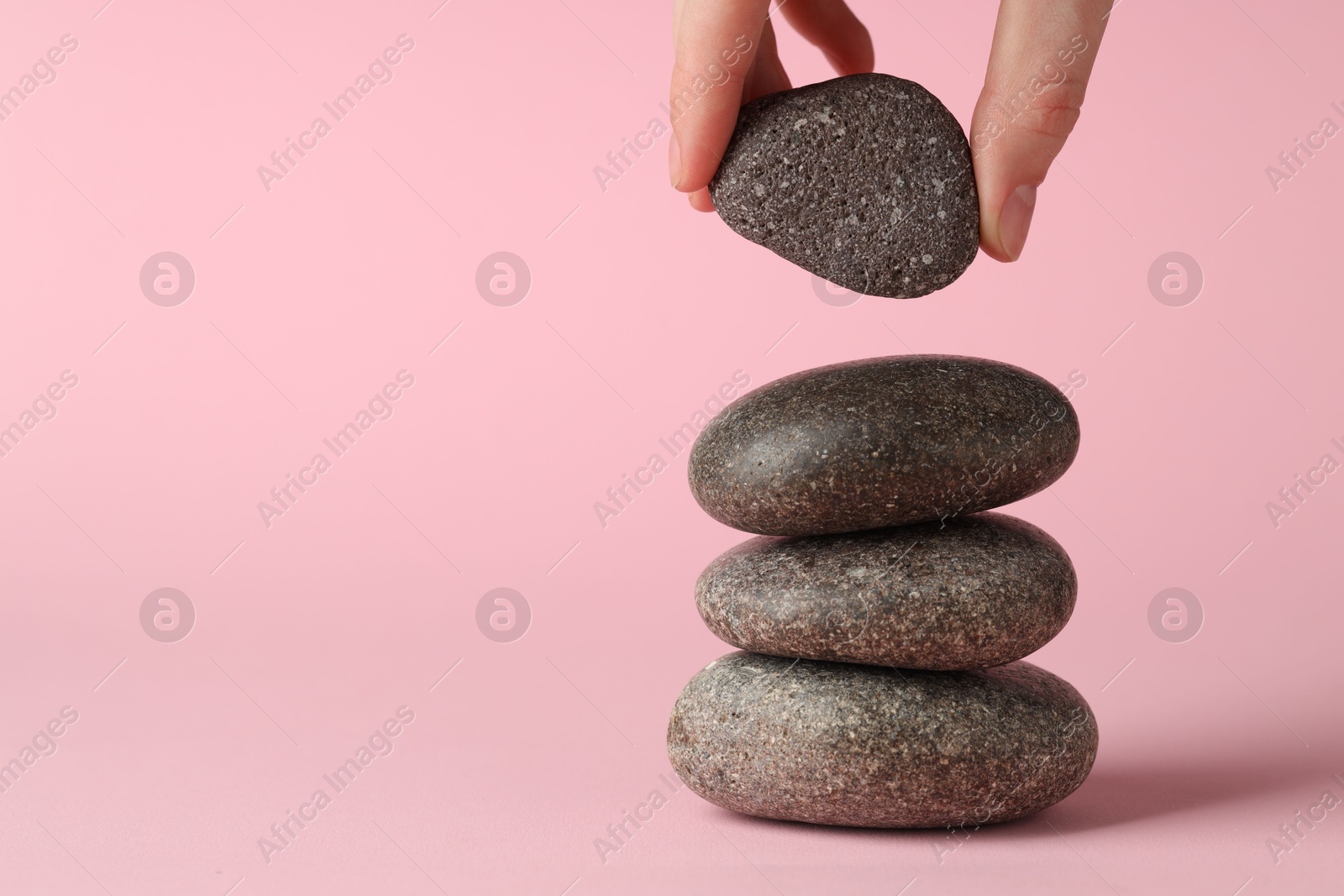 Photo of Harmony and life balance. Woman making stack of stones on pink background, closeup. Space for text