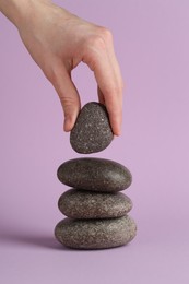 Photo of Woman making stack of stones on lilac background, closeup. Harmony and life balance