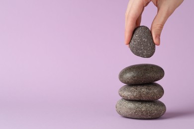 Photo of Harmony and life balance. Woman making stack of stones on lilac background, closeup. Space for text