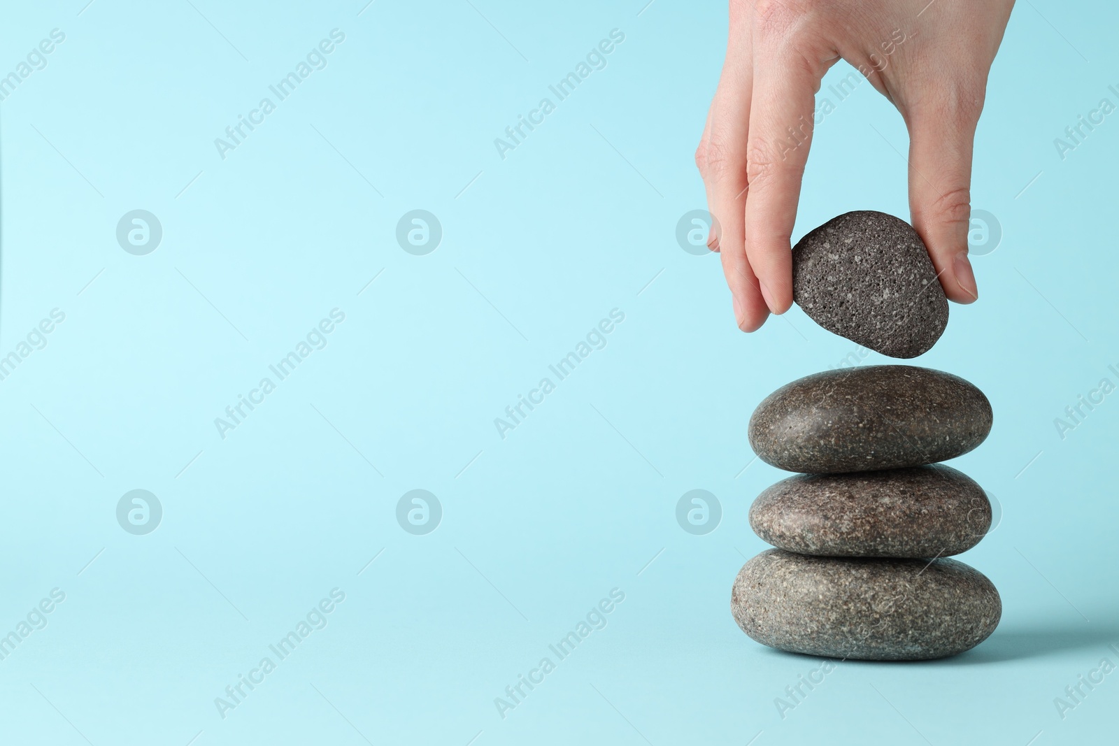 Photo of Harmony and life balance. Woman making stack of stones on light blue background, closeup. Space for text