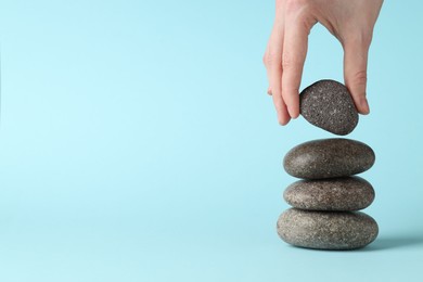 Photo of Harmony and life balance. Woman making stack of stones on light blue background, closeup. Space for text