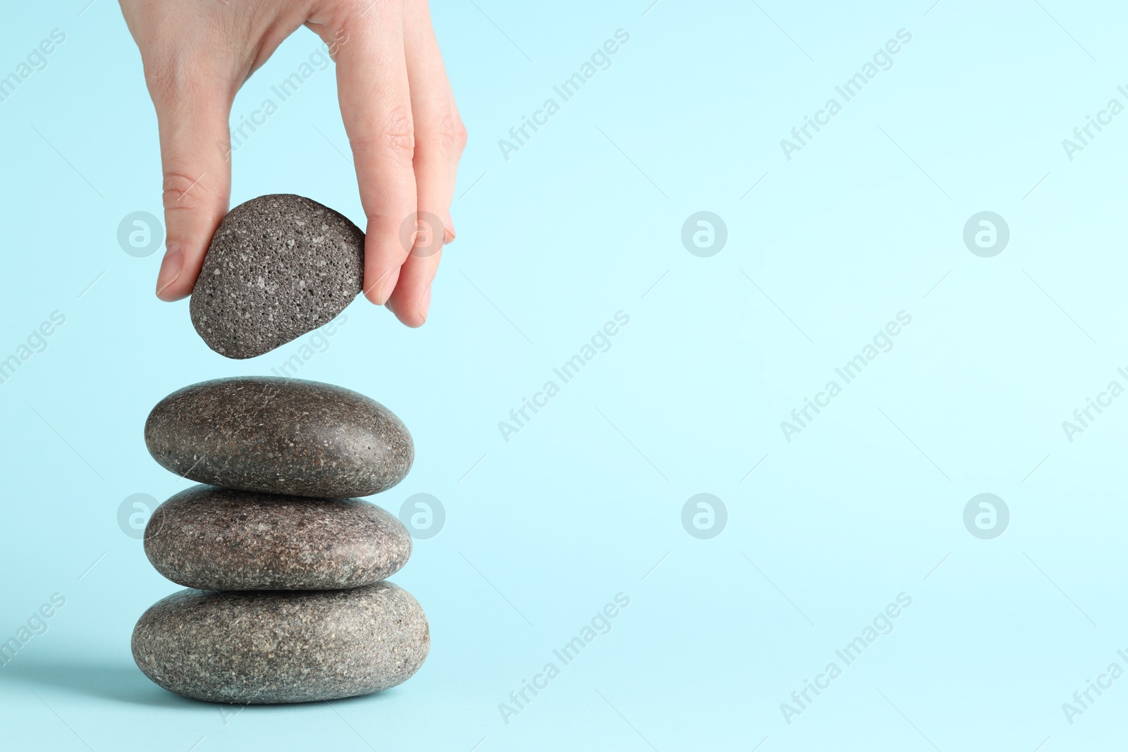 Photo of Harmony and life balance. Woman making stack of stones on light blue background, closeup. Space for text