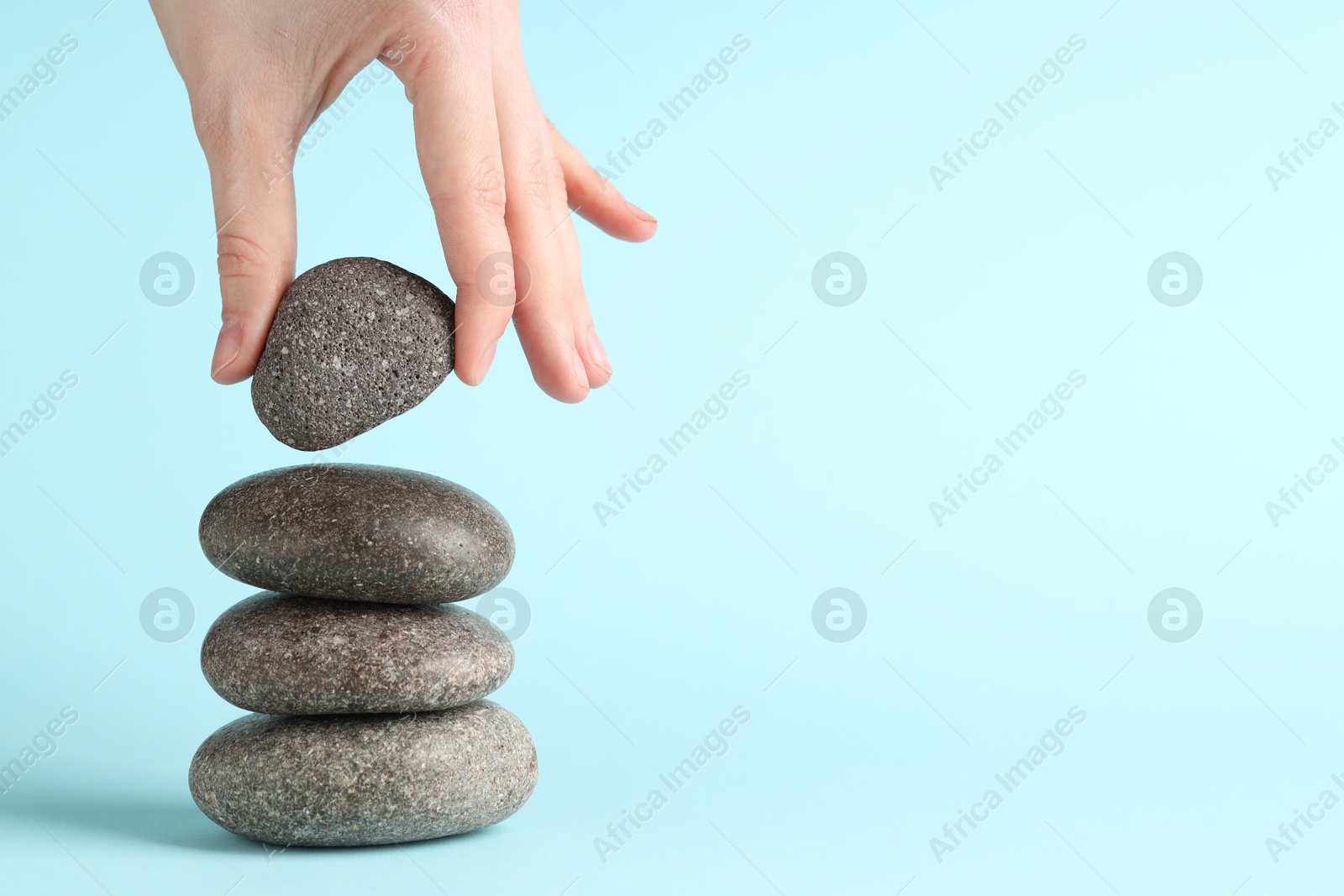 Photo of Harmony and life balance. Woman making stack of stones on light blue background, closeup. Space for text