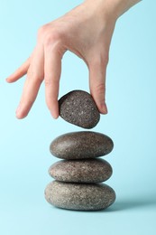 Photo of Woman making stack of stones on light blue background, closeup. Harmony and life balance