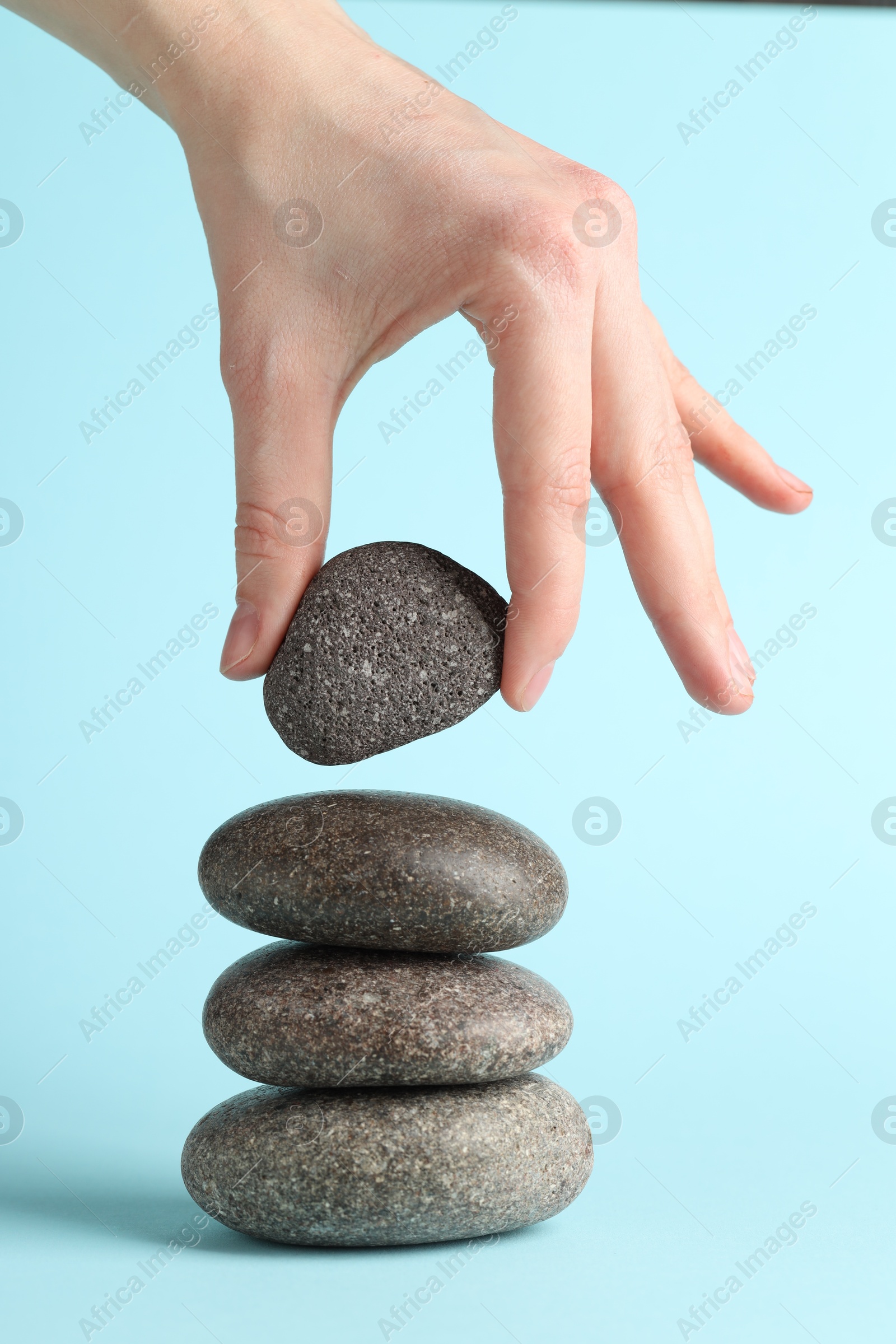 Photo of Woman making stack of stones on light blue background, closeup. Harmony and life balance