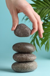 Photo of Woman making stack of stones on light blue background, closeup. Harmony and life balance